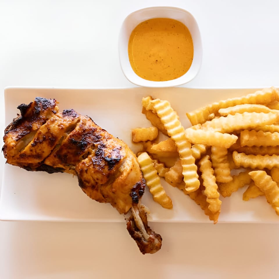A grilled chicken leg quarter with crinkle-cut fries and a side of orange sauce on a white plate.