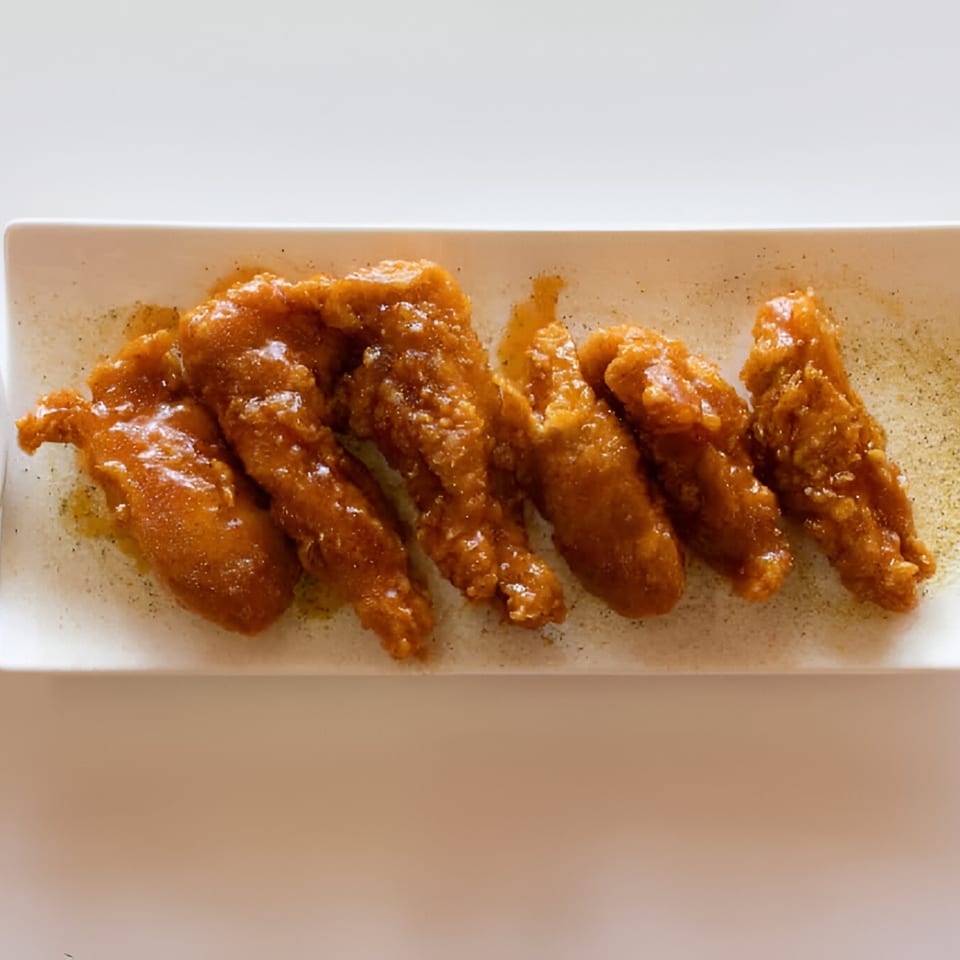 Six crispy, glazed chicken wings dusted with pepper, served on a white rectangular plate.