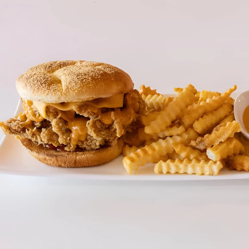 A Chick Fry chicken sandwich with melted cheese and crinkle-cut fries on a white plate.