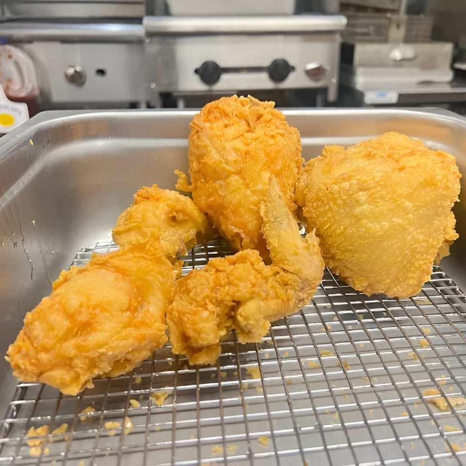 Golden-brown fried chicken pieces resting on a metal rack in a stainless steel pan.